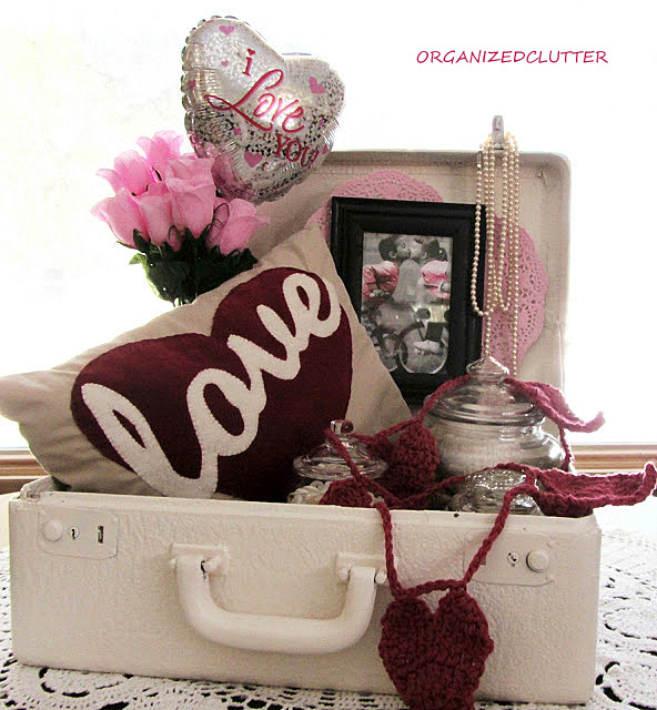 a valentine s day love suitcase, repurposing upcycling, seasonal holiday d cor, valentines day ideas, Jars of buttons and thread the pillow a crocheted heart garland a framed card Dollar Tree balloon roses paper heart doily and pearls complete my suitcase vignette
