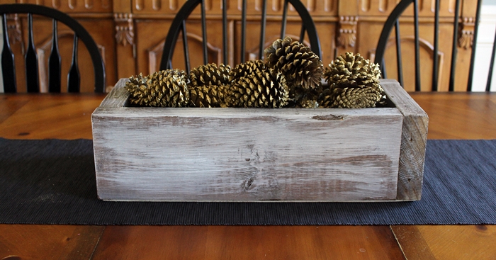 caixa caiada de branco com centro de mesa de natal de pinhas douradas