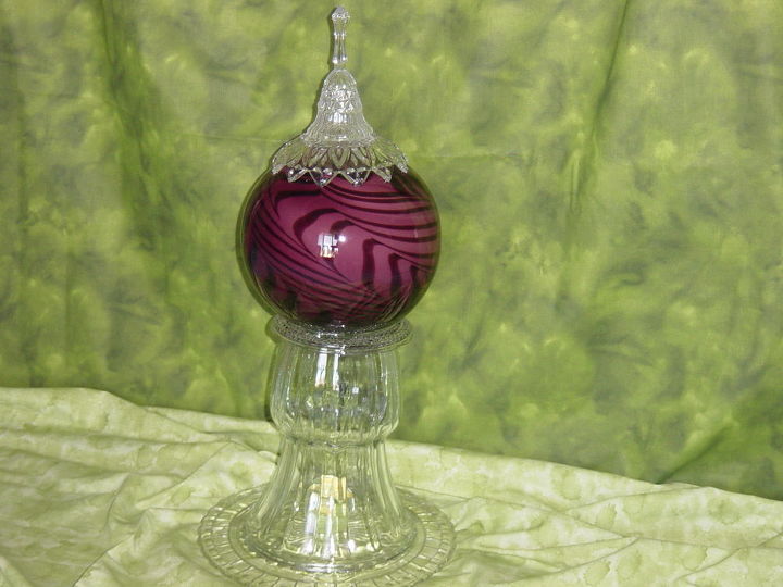 repurposed glass, A gazing ball made from a bell a bowl a heavy purple art glass vase atop a heavy inverted clear vase with a yellow flowered paper weight nestled inside and mounted on a cake platter It is over 2 feet tall Assembled by Nita Hooper
