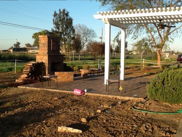 landscape help around our new outdoor living space, gardening, landscape, outdoor living, The photo is taken from the left side of the paver patio so hopefully you can see the areas on either side that need landscaping Right now there is wood piled on either side of the fireplace which could should be moved The area is defined somewhat by a line of bushes in a half circle There is temporary electric fencing around that to keep the horse from camping on the patio The road which is pretty busy as the dump is on it is directly behind the fireplace hence the need for some privacy planting We have oleanders planted outside the chain link fence but they have never grown huge like everyone else s in the world