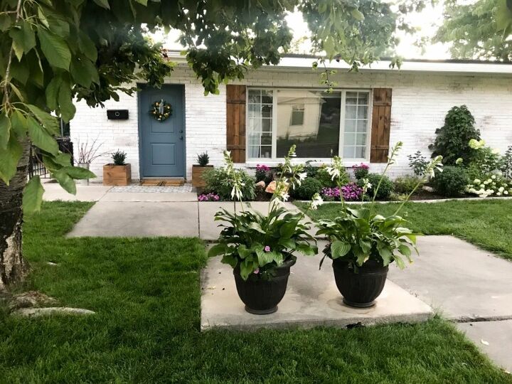 how to hang wood shutters on brick, white brick house with designed landscape blue door and wood shutters