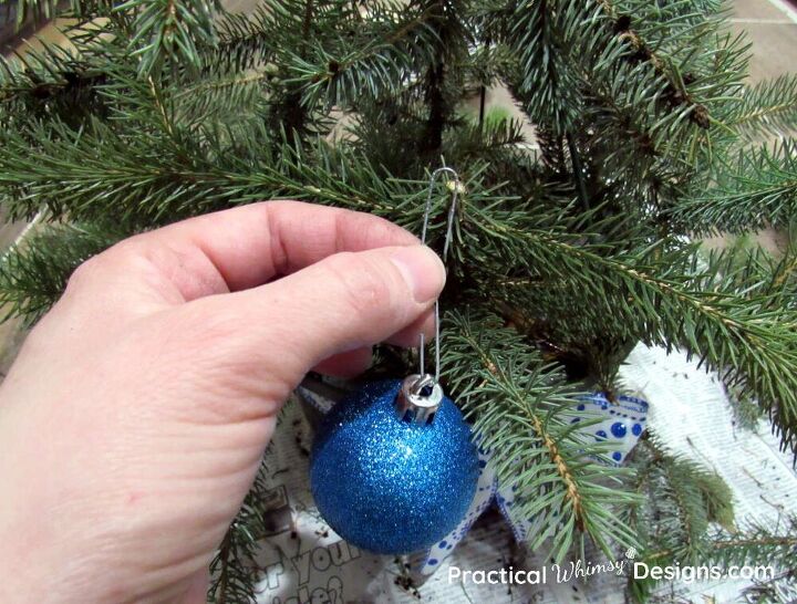 cesta de pino navidea diy, Adorno azul colgado a mano en una rama de pino