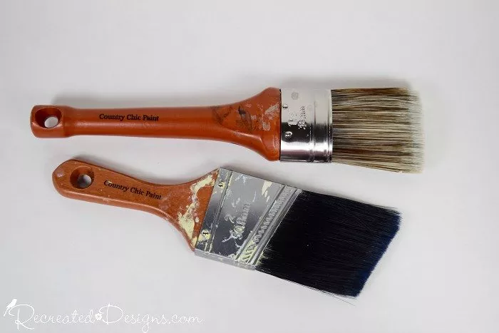 a step by step guide on how to paint a room, Two wood handled paint brushes laying on a white surface