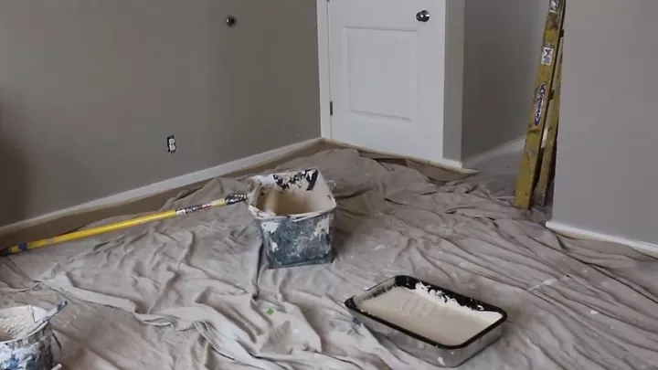 a step by step guide on how to paint a room, room covered in a drop cloth and paint bucket