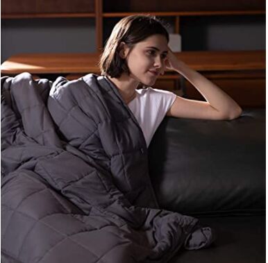 las 7 mejores mantas trmicas para confortar a los que duermen con calor, una mujer con camisa blanca en un sof de cuero con una manta gris ponderada sobre ella