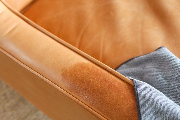 como limpar mveis de couro para ficarem como novos, um pano cinza limpa uma mancha escura em uma cadeira de couro marrom claro
