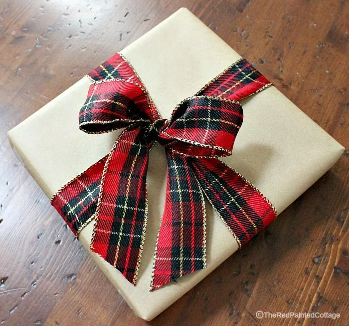 how to wrap a present, tan wrapped gift with red and green plaid ribbon tied in a bow