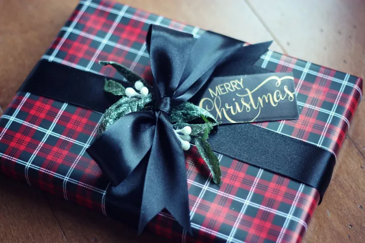 how to wrap a present, gift wrapped in green and plaid wrapping paper with black ribbon tied in a bow and Merry Christmas gift tag