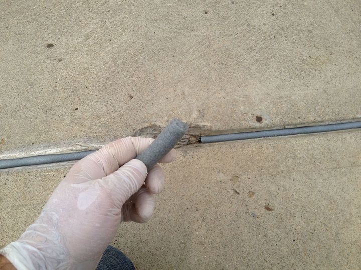how to fix cracks in a concrete patio yourself, a gloved hand places poly foam into a crack in concrete