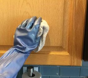 cmo limpiar los armarios de cocina de cualquier tipo de material, mano con guante de goma limpiando la puerta del armario de madera de la cocina con una toalla