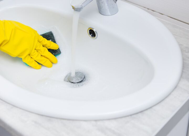 how to deep clean a bathroom, rubber gloved hand using sponge to wipe sink basin