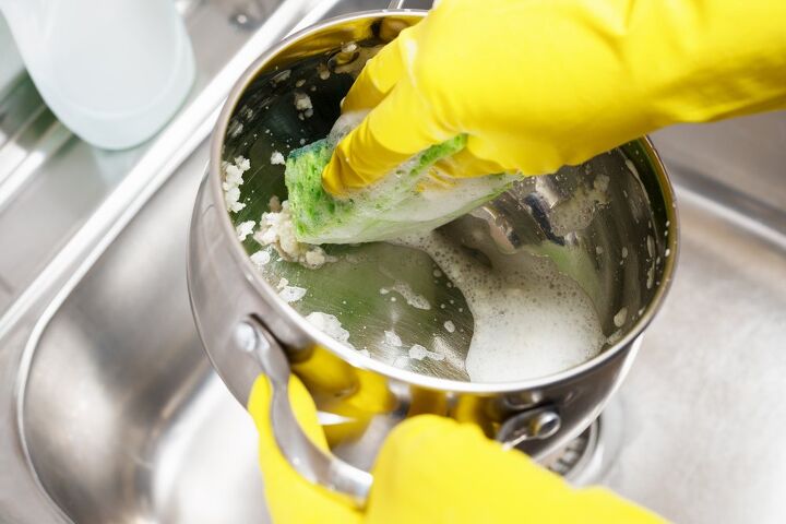 como limpiar correctamente las sartenes de acero inoxidable, manos con guantes de goma limpiando con agua jabonosa una olla de acero inoxidable