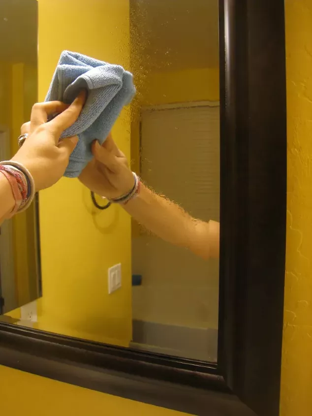 how to clean a mirror to a streak free perfection, hand wiping blue cloth against mirror