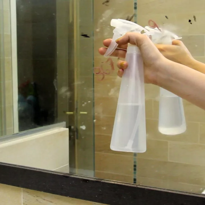 how to clean a mirror to a streak free perfection, hand spraying clear spray bottle onto dirty mirror