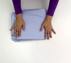 the ultimate guide to folding a fitted sheet properly, Hands folding purple fitted sheet