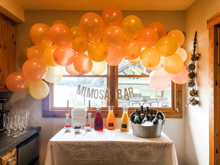 how to make a balloon garland to level up your next party, orange and pink balloon garland hanging over window