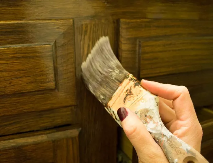 how to stain wood, hand moving brush against wood cabinet
