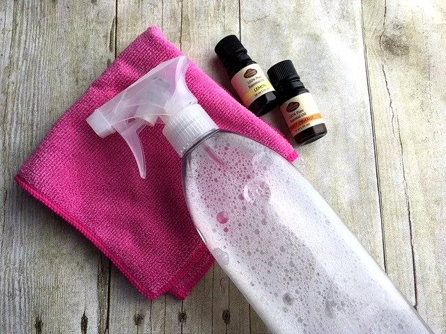 how to clean and disinfect granite countertops, cleaning solution in clear spray bottle laying on pink towel next to essential oils