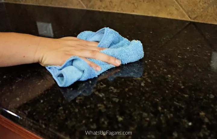 how to clean and disinfect granite countertops, hand wiping down granite countertop with blue towel