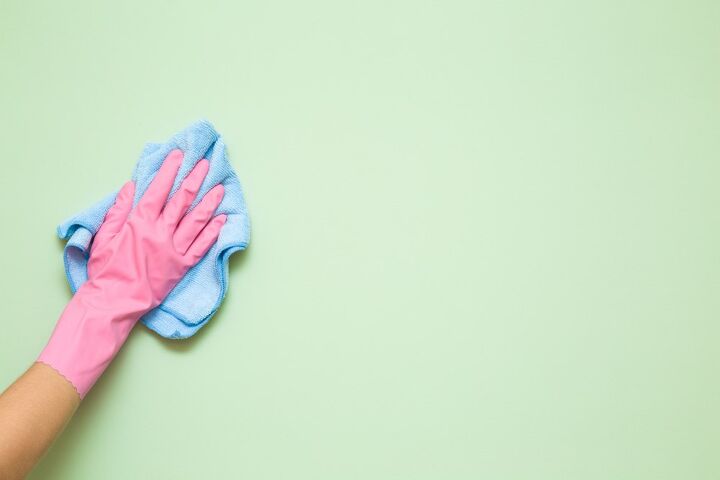 como limpiar las paredes con pintura plana y deshacerse de las marcas persistentes, Mano con guante de goma rosa usando una toalla azul para limpiar una pared pintada de verde