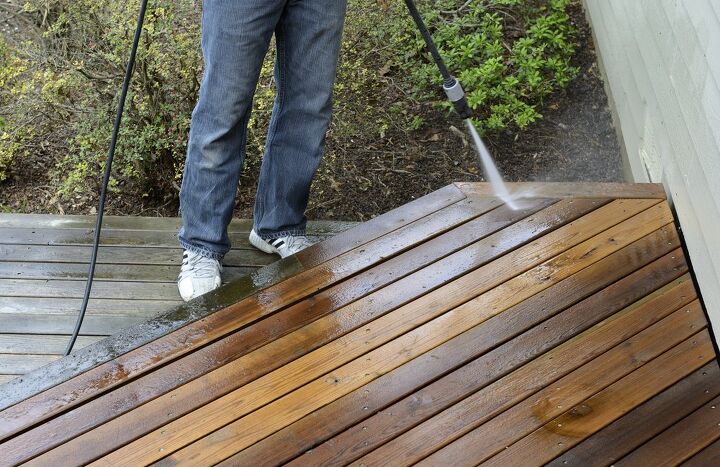 this is how to pressure wash a deck the right way, person in jeans power washing the edge of a wood deck