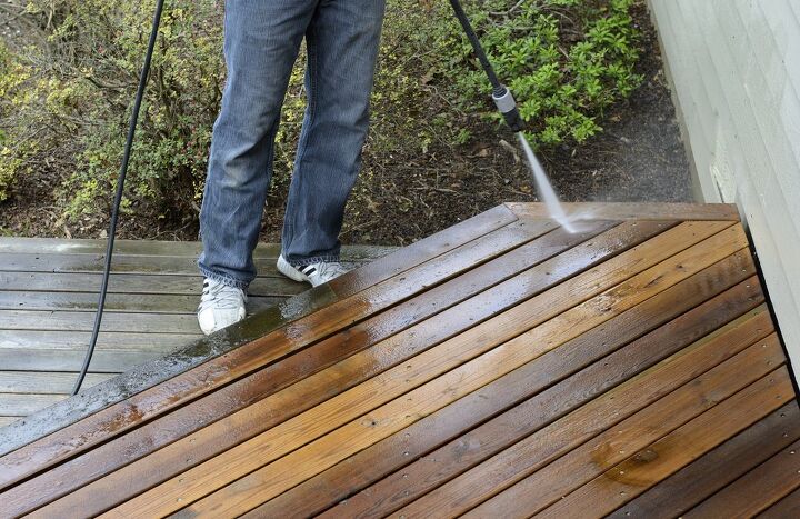 this is how to pressure wash a deck the right way, person in jeans power washing the edge of a wood deck