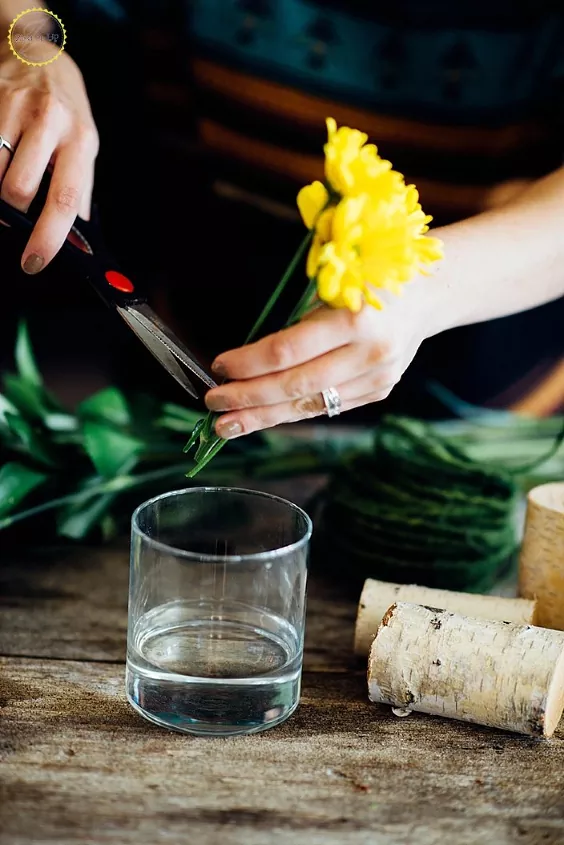 how to make artificial flower arrangements look more realistic, hand using scissors to snip stem of yellow faux flower