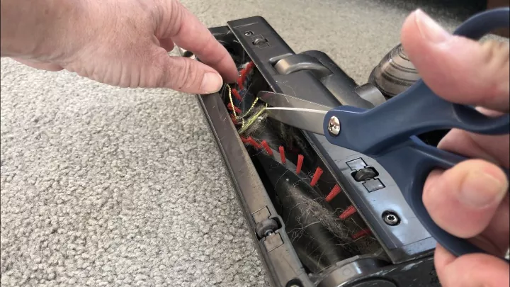 how to clean a vacuum, person using scissors to clean vacuum brush roller