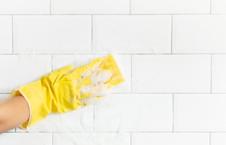 Yellow gloved hand and sponge wiping white tile