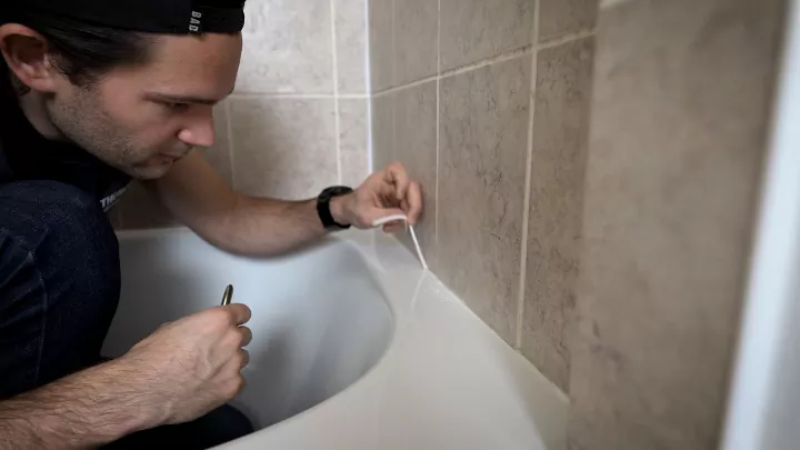 how to remove caulk when it s old and dingy, man removing caulk from bathtub