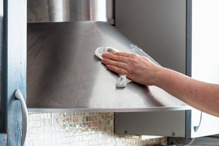 how to clean a range hood filter, person using towel to wipe outside of range hood