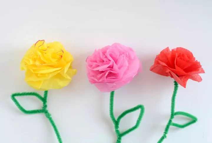 how to make tissue paper flowers, one yellow one pink and one red tissue paper flower with green stems
