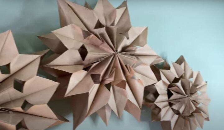 how to make this beautiful rustic paper bag snowflake craft, Three paper bag snowflakes hanging on a wall