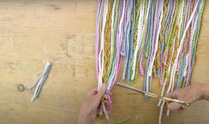 here s how to make gorgeous boho rainbow wall decor, Trimming the bottom of the yarn