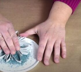 how to make festive glitter toilet paper roll snowflakes, Dipping the sticky side of the snowflake into blue glitter