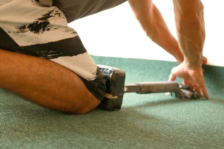 guia completo sobre como esticar um tapete voc mesmo, pessoa usando uma joelheira para empurrar o tapete