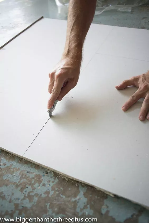 cmo quitar el revestimiento de azulejos y reemplazar la pared de yeso si es necesario, persona usando un cuchillo para cortar los paneles de yeso