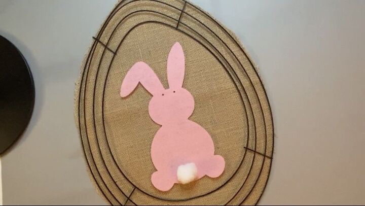 photo of a pink rabbit with a cotton for a tail sitting on top of an egg-shaped burlap cutout surrounded by wifreframe