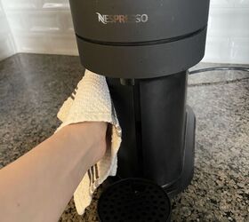 how to clean a nespresso machine in a few easy steps, Hand using towel to wipe down black Nespresso machine