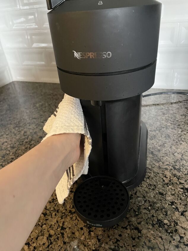 how to clean a nespresso machine, Hand using towel to wipe down black Nespresso machine