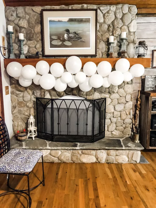 how to make a balloon garland to level up your next party, white balloon garland hanging on fireplace mantel