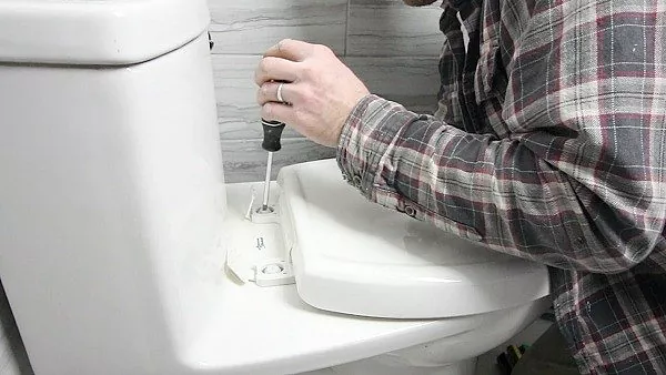como substituir um assento de vaso sanitrio de forma rpida e fcil, pessoa usando uma chave de fenda para desaparafusar a tampa e o assento do vaso sanit rio
