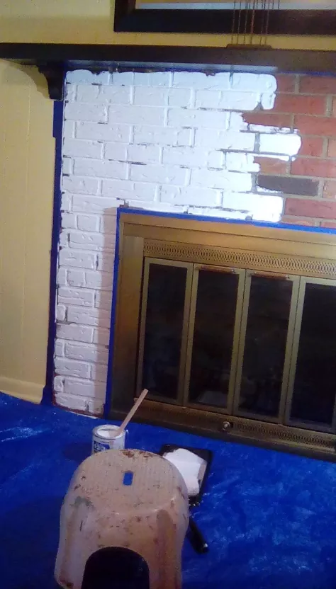 how to paint a brick fireplace, brick fireplace with painter s tape and half painted with white paint