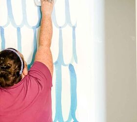 cmo colgar papel pintado con pasta, mujer sujetando un alisador de papel pintado sobre una pared empapelada en azul y blanco