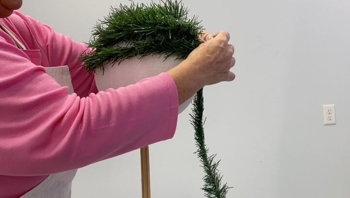 7 simple steps to make this festive diy christmas topiary, Wrapping a Styrofoam ball with a faux greenery garland