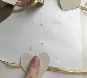 guirnalda de lazos y corazones de papel, El dedo de una mujer presionando dos corazones pegados a una cinta para hacer una guirnalda de coraz n y cinta de papel