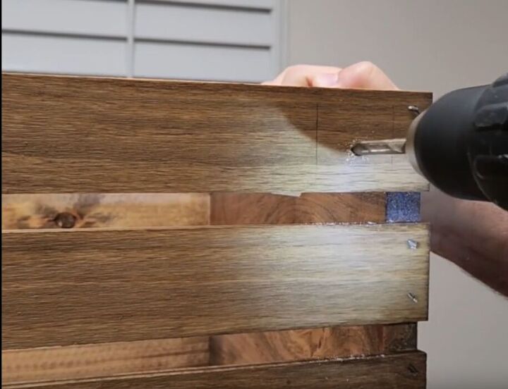 how to make an impressive rustic diy wood crate coffee table, Drilling a hole at the bottom of the wood crate coffee table to insert the leg pieces