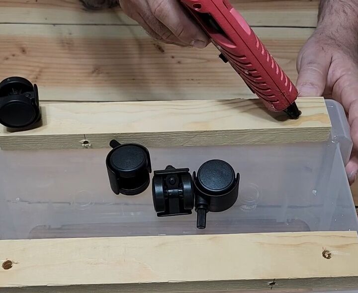 3 easy steps to a stylish diy plastic storage bin makeover, Adding hot glue to the predrilled holes for the caster wheels