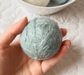 cmo hacer bolas de lana sostenibles para la secadora bricolaje fcil, una bola de lana azul menta hecha a mano en la mano de Caley sobre un fondo blanco con un cuenco blanco con m s bolas de lana DIY sentado detr s de ella