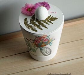 cmo hacer un encantador portabolsas de t, Maceta blanca decorada con una servilleta decorativa flores y hojas de papel y tapa redonda de madera con cuenta de madera